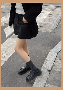 Détail de mocassins noirs à plateforme avec boucle et jambières grises en tricot