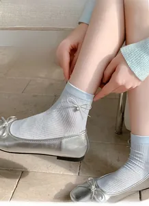 Dettaglio di calze azzurre a coste con fiocco, ciondolo a cuore e scarpe ballerine