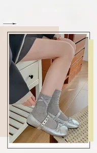 Dettaglio di calze grigie in maglia con fiocchi viola abbinate a scarpe Mary Jane argento