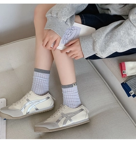 Close-up of beige sneakers with silver stripes paired with striped crew socks