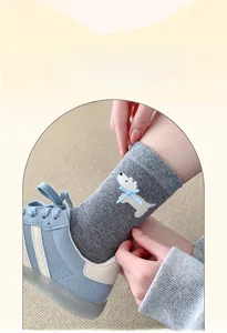 Detail of grey cotton sock featuring white terrier embroidery and light blue 3D bow