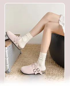 Detail von rosa Clogs mit Schnallen und weißen Zopfstricksocken auf einem Teppich