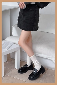 Détail de chaussettes hautes en coton blanc avec mocassins noirs et jupe en jean