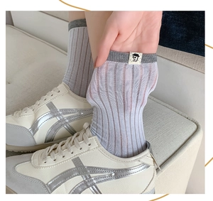Detail of grey crew socks with cartoon label paired with retro sneakers and stripe texture