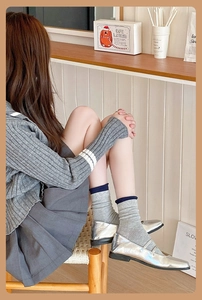 Détail de chaussettes en maille grise avec bord bleu et chaussures Mary Jane argentées