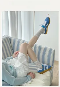 Close-up of white striped mesh socks paired with blue retro trainers on a sofa