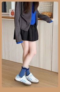 Détail de chaussettes bleues à bords ondulés avec jupe plissée marine et baskets blanches