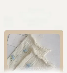 Dettaglio di calze color crema con motivi floreali blu e bordo elastico a volant
