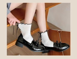 Close-up of black patent leather loafers with double bows and white lace ribbon socks