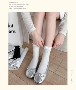 Detail of white crew socks with ruffle cuffs and pearl bow accents worn with ballet flats
