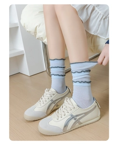 Detail of light blue crew socks with lace trim and cream leather sneakers on wood floor