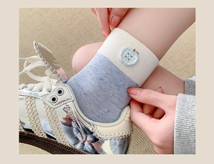 Detail of color-block knit socks with a plaid apple button and silver sneakers