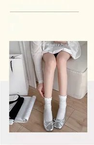 Close-up of white mid-calf socks with ruffle trim and silver bow detail worn with silver shoes