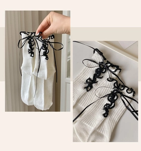 Close-up of white lolita socks with black lace trim and bow ribbons in soft cotton