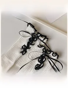 Detail of white knit socks featuring black ruffle trim and silk satin bow decorations