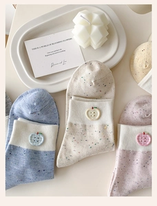 Detail of knit socks with colorful speckles and an apple button decoration
