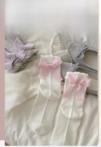 Close-up of cream Lolita socks with pink bow tie and breathable mesh texture on bed