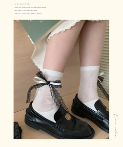 Detail of white ribbed crew socks featuring black lace trim and satin bow accents