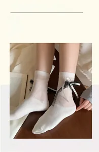 Detail of ballet style white mid-calf socks with black lace and ribbon bow accents