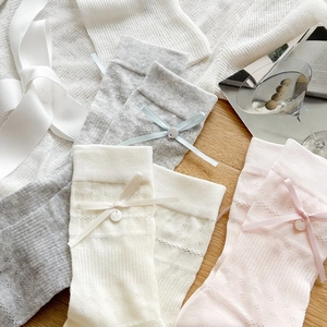 Detail of hollow-knit mesh crew socks with silk bows and pearl buttons in soft colors