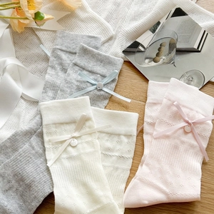 Detail view of lace knit socks with ribbon bows and pearl buttons in soft pastel colors