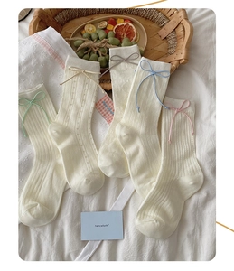Détail de chaussettes en résille blanc cassé avec nœuds colorés et motifs cœurs