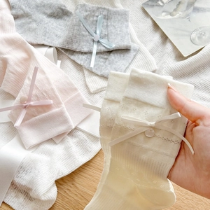 Detailed view of hollow knit socks with bow and button accents in pastel colors