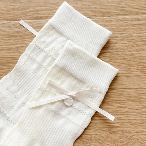 Detailed knit texture of cream baby socks with ribbon bow and pearl button detail
