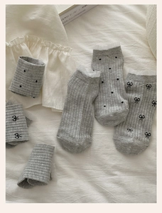 Detail of light gray socks featuring white lace trim, polka dots and black bow accents