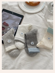 Detail of four pairs cotton socks with bow embroidery on white wrinkled sheet bedding
