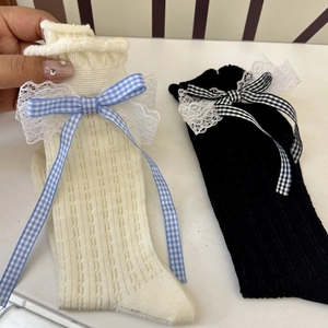 Detailed view of lace trim and plaid bows on white and black cotton knit mid-calf socks