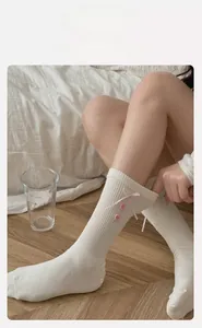 Detail of white cotton mid-calf socks with pink bows and decorative buttons for women