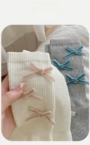 Detail of cream and grey mid-calf socks with velvet bows and ribbed cotton texture