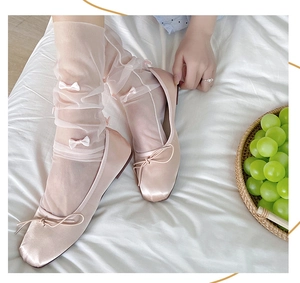 Detail of pink satin ballet flats with square toe and white mesh bow socks on bed