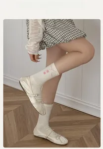 Detail of white ribbed crew socks with pink bow and button paired with ballet flat shoes