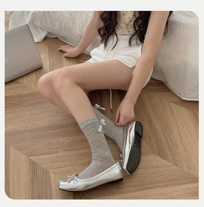 Détail de chaussettes grises à côtes avec nœud bleu et ballerines argentées