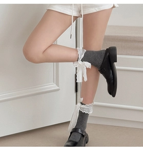Detail of grey cotton socks with white lace bows and ruffled cuff styled with shoes