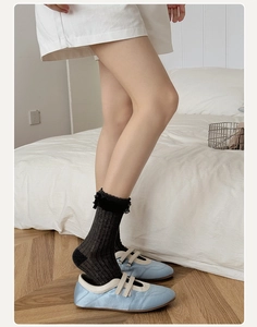 Detail of white lace ruffled socks paired with satin ballet flats in a cozy room setting