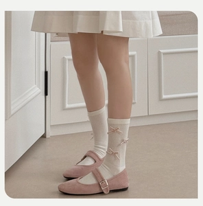 Detail of white ribbed crew socks featuring a velvet bow paired with pink Mary Jane shoes