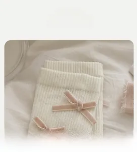 Macro view of white ribbed knit socks with a soft pink velvet bow and elastic cuff