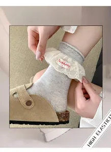 Détail de chaussettes en maille gris clair avec bord en dentelle blanche et lettrage