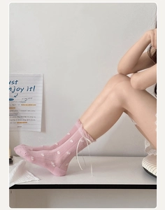 Close-up of pink crew socks featuring white heart patterns and delicate ribbon bows