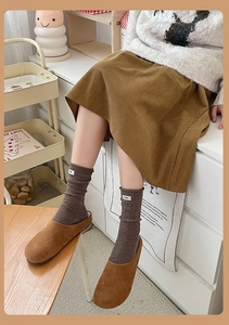 Detailed close-up of brown ribbed wool socks with egg label and cozy suede mule slippers