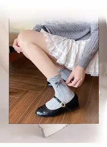 Detail of grey cable knit socks with bow paired with black Mary Jane shoes