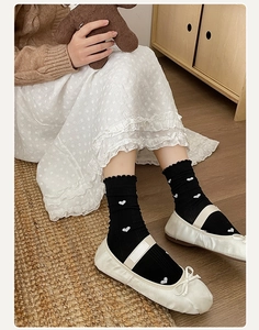 Détail de chaussettes mi-mollet noires à cœurs blancs, bords volantés et Mary Janes
