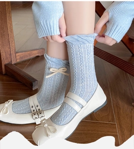 Detail of light blue cable knit socks with white ribbon bow and frilly cuff design