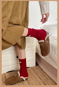 Detail of red ribbed wool socks with white label worn with brown suede fur-lined clogs