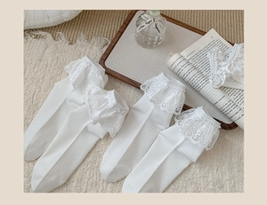 Detailed view of white cotton socks with elegant lace embroidery on a soft beige carpet
