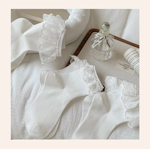 Detailed view of white cotton ribbed socks featuring layered lace trim on a white fabric