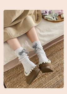 Detailed close-up of white ribbed knit cashmere socks with a decorative grey bow detail